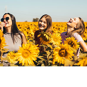 3 jeunes filles d'un vingtaine d'années s'amusent et rigoles dans un champ de tournesol.